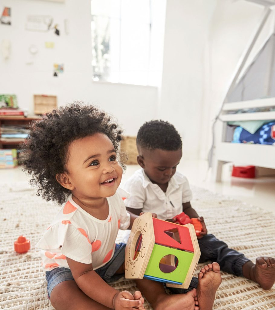 Zwei Kinder spielen mit Spielzeug am Zimmerboden